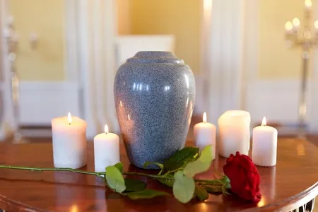 Urne cinéraire en granit gris entourée de bougies allumées et d'une rose rouge