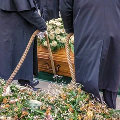Porteurs funéraires descendant un cercueil en bois orné de fleurs blanches au moyen de cordes
